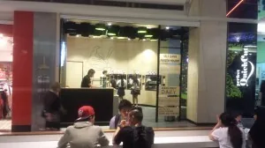The finished CRAVE store seen from across the shopping centre walkway, its signage and interior lighting lit in the evening