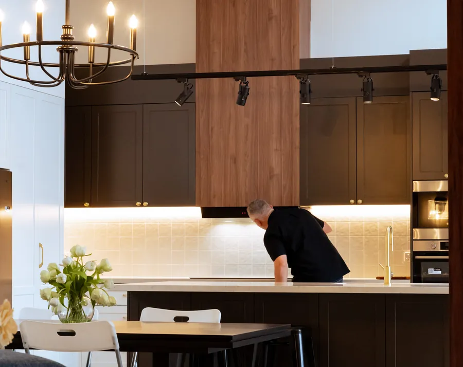 A renovated kitchen lit by track spotlights, under-cabinet LED strip lighting and a chandelier over the dining table