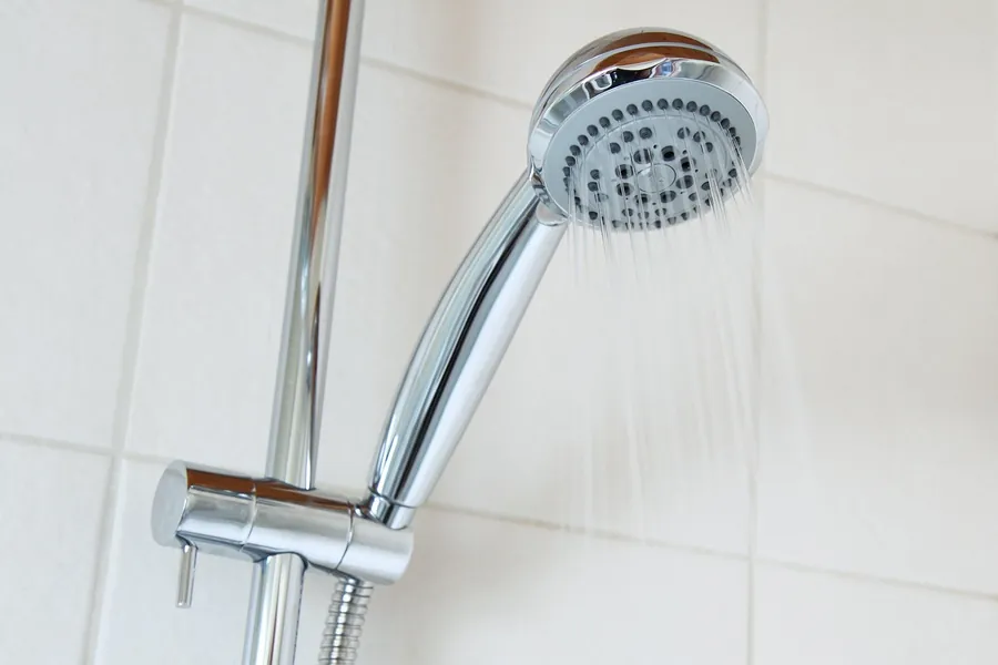 running water from shower head in white tile bathroom