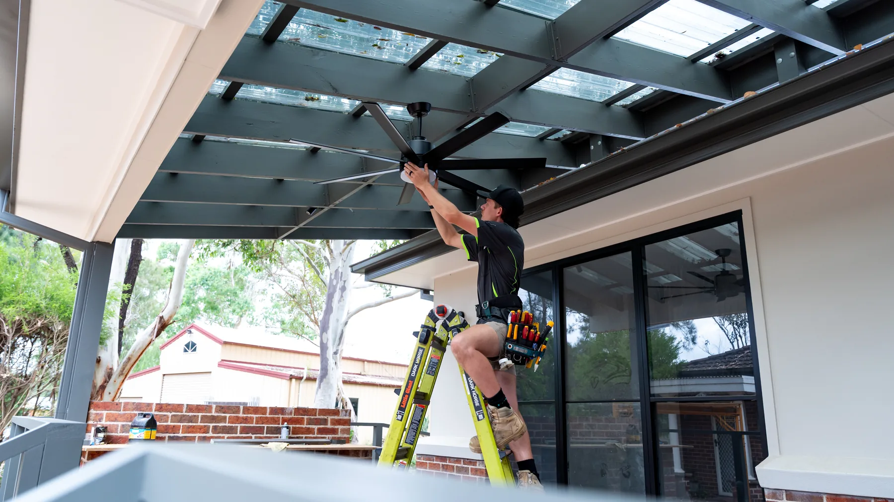 Electrician installing a fan under a covered patio