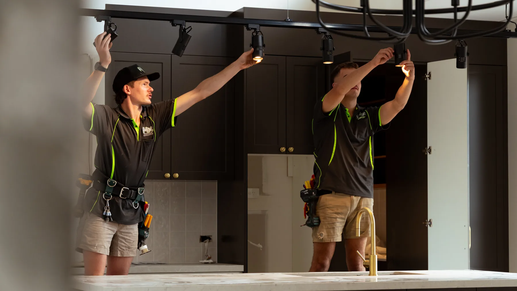 Electricians fitting cabinetry lighting in a kitchen