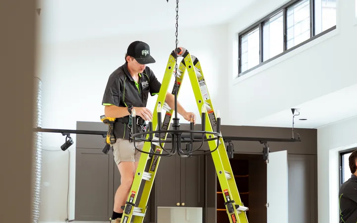 Electrician installing a pendant light from a ladder