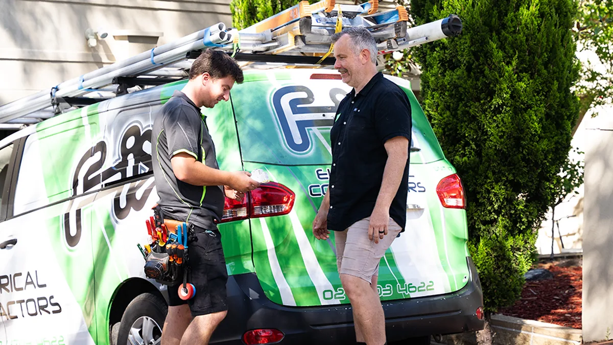 Fix Electrical electrician showing a light fitting to a customer beside the branded van